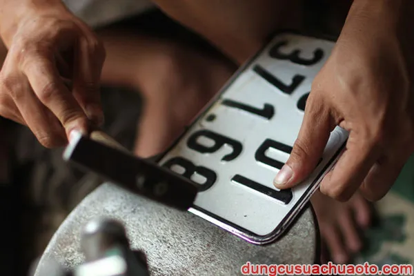 Cận cảnh quá trình đặt miếng mica trong suốt lên trên bề mặt biển số xe máy trước khi tiến hành ép nhiệt và gò viền.