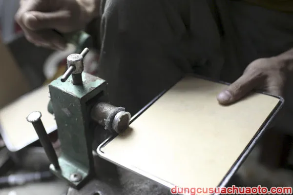 Sử dụng búa chuyên dụng để gò các mép của khung ốp, ép chặt miếng mica vào tấm biển số, đòi hỏi kỹ thuật và sự chính xác cao.