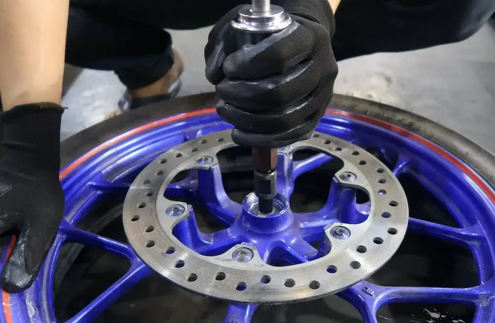 Kỹ thuật viên kiểm tra trục bánh xe máy để xác định dấu hiệu hư hỏng của vòng bi, liên quan đến giá bạc đạn bánh sau xe máy.