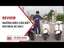 Một chiếc xe ga 50cc màu đỏ trắng đang đậu bên ngoài một tòa nhà chung cư